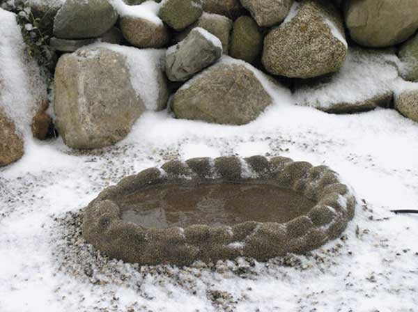 Brown coated fake rock birdbath sitting snow