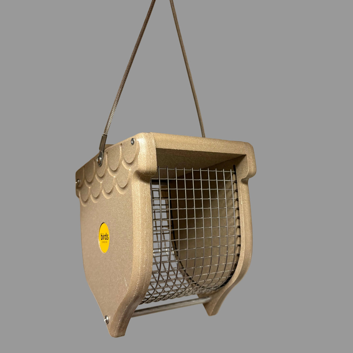 A hanging bird feeder made of beige plastic with a metal wire mesh front and a small yellow logo sticker, suspended by two metal wires.
