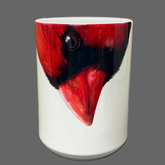 A white ceramic mug featuring a realistic printed illustration of a red cardinal bird face, set against a gray tablet case and pegboard background.
