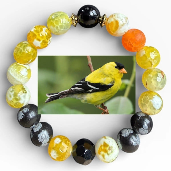 A circular beaded bracelet arranged in a ring on a white background, with a central inset photo of a goldfinch perched on a branch. The bracelet features faceted beads in yellow, black, white marbled patterns, and orange, with small gold spacer accents.