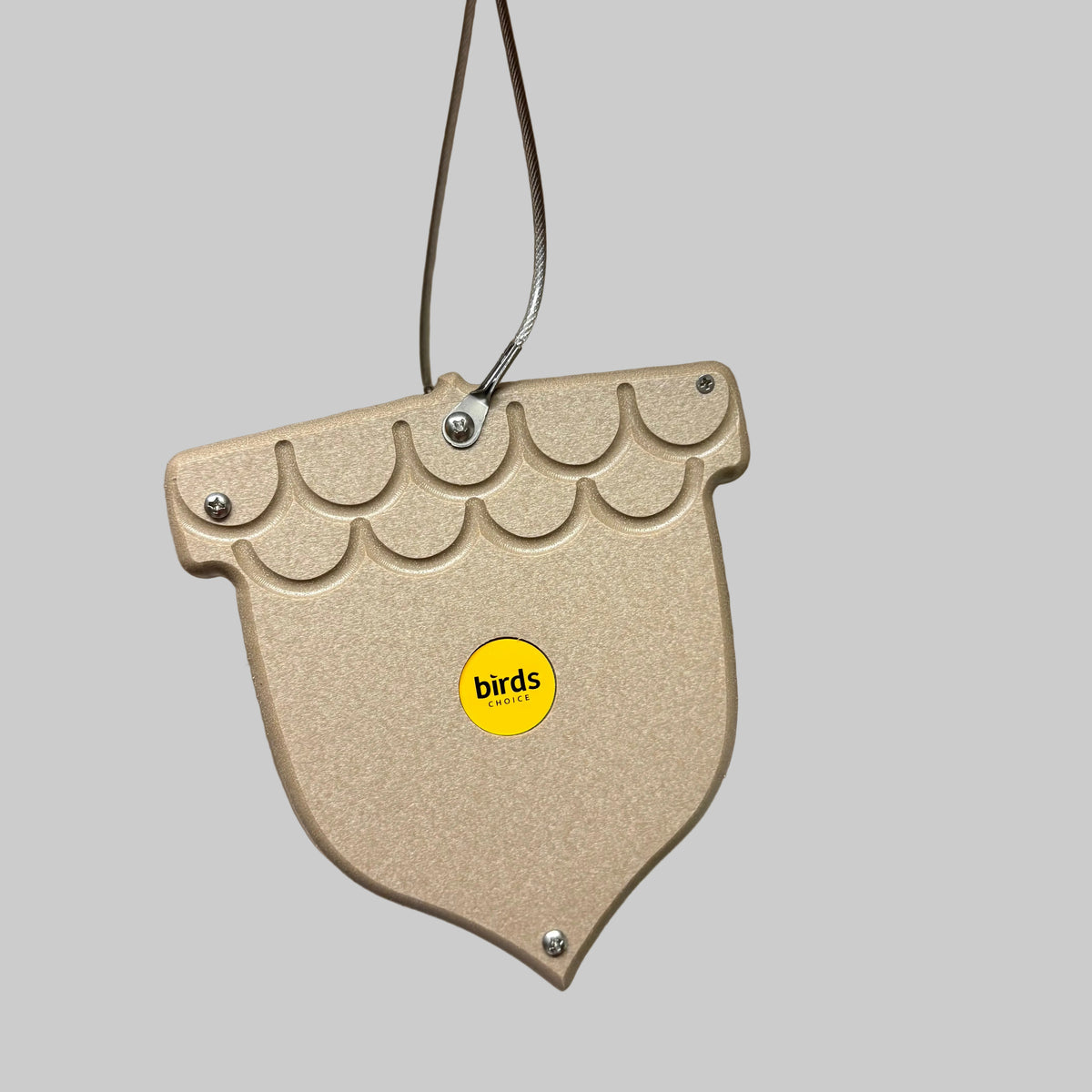 A beige textured bird feeder hanging from a metal wire, featuring a scalloped top edge, silver screws, and a yellow circular sticker with the brand name 'birds'.
