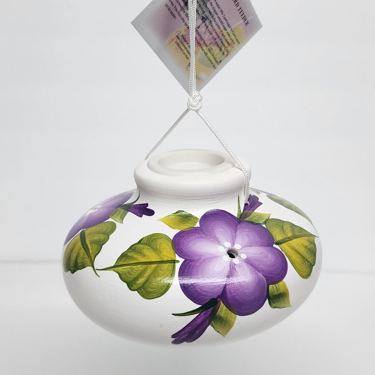 purple posy flowers on a white ceramic hummingbird feeder